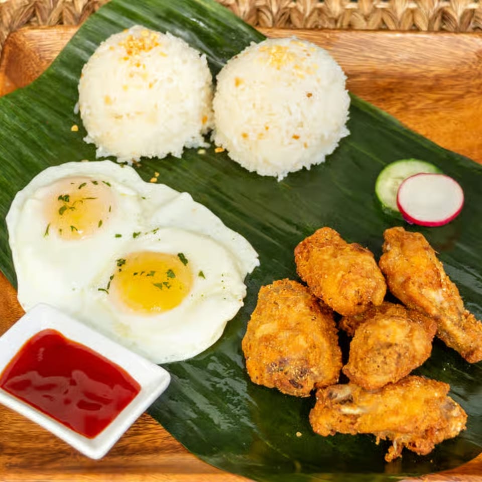 Filipino breakfast with fried chicken, two fried eggs, garlic rice, and ketchup on a banana leaf.