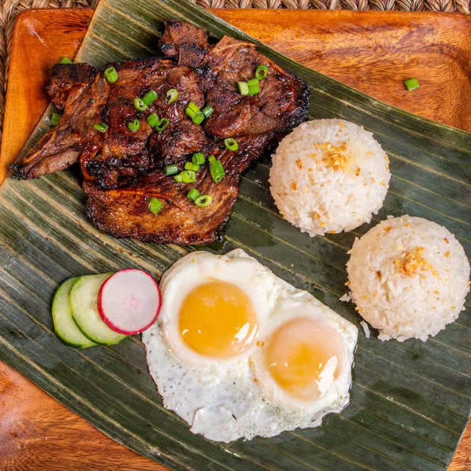 Filipino Lutong Bahay meal with grilled meat, two fried eggs, two scoops of rice, and sliced vegetables.