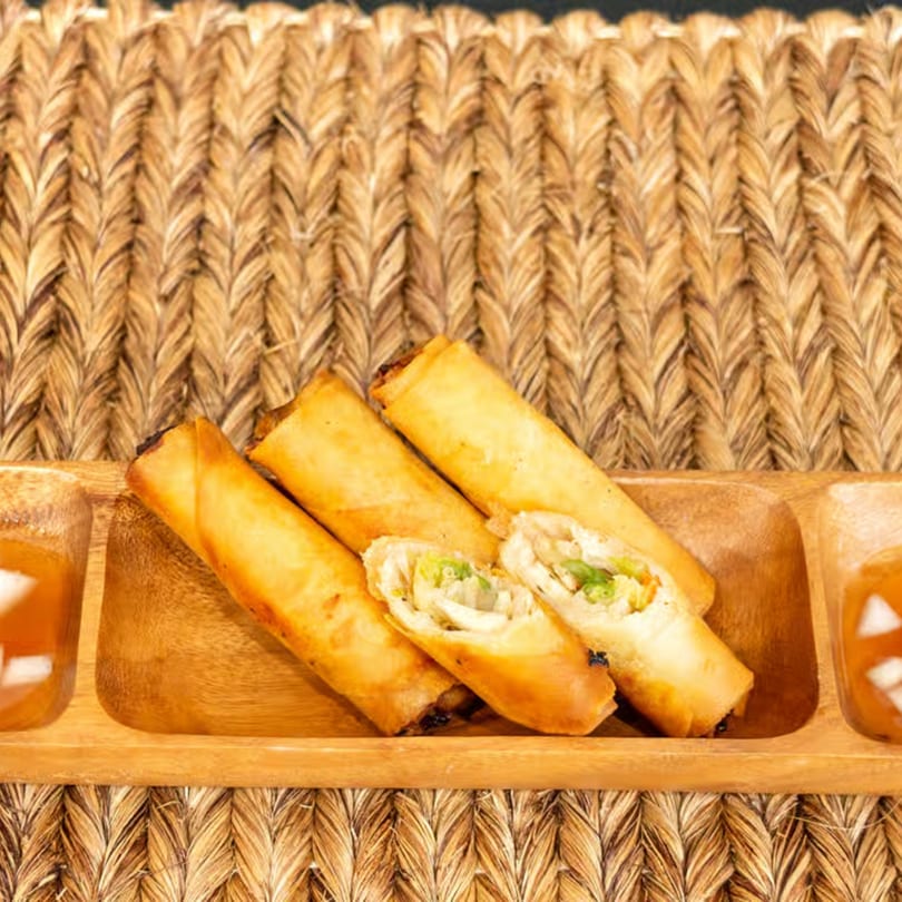 Lutong Bahay's golden-fried Filipino lumpia spring rolls, one cut open, served with dipping sauce.