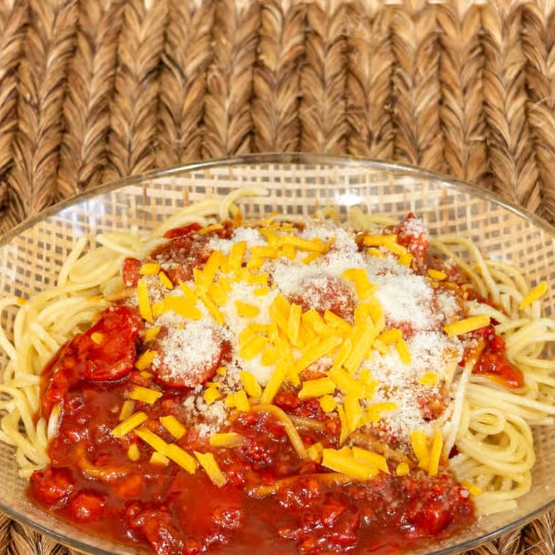 Filipino-style spaghetti with sweet tomato sauce, hot dogs, shredded cheddar, and grated cheese.