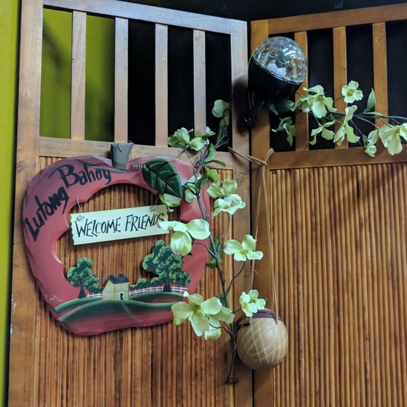 A wooden apple-shaped sign with "Lutong Bahay Welcome Friends" hangs on a bamboo wall.